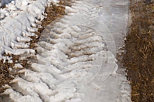 Tractor wheel tracks on melting snow and dark ground