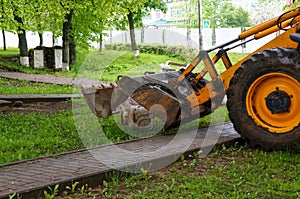 A tractor on wheels with a bucket on a city street performs