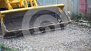 The tractor works during the restoration of the loosening crushed stone road. The excavator bucket leveling the road