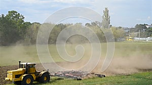 Tractors cultivating field under a blue sky.