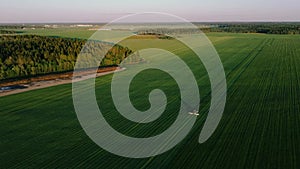 Tractors mow green grass in the fields aerial shot in summer at sunset