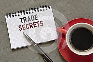 TRADE SECRETS - words in a white notebook on a gray background with a pen and a cup of coffee