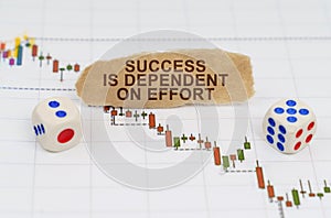 On the trading charts, there are dice and pieces of paper with the inscription - SUCCESS IS DEPENDENT ON EFFORT