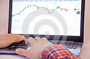 Trading on the exchange. Men`s hands in a plaid shirt at a laptop. On-screen rates, promotions. Schedule. Wins are losses. Part o