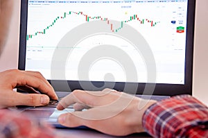 Trading on the exchange. Men`s hands in a plaid shirt at a laptop. On-screen rates, promotions. Schedule. Wins are losses. Part o