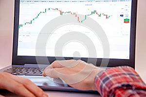 Trading on the exchange. Men`s hands in a plaid shirt at a laptop. On-screen rates, promotions. Schedule. Wins are losses. Part o