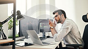 Trading strategy. Successful young trader in eyeglasses looking at analyzing trading charts on computer screens in while