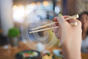 Tradition, bamboo chopsticks and hand of a person eating Japanese food at a restaurant for nutrition. Closeup of a woman