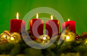Traditional advents wreath with 4 flames on the burning candles in front of a green background.