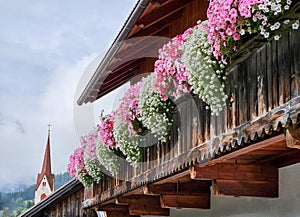 Traditional alpine style house with colorful floral arrangement on balcony in picturesque village