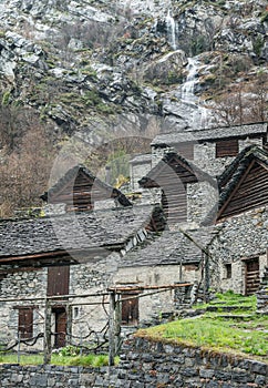 Traditional alpine village with many small wooden and stone houses and a mountain waterfall backdrop