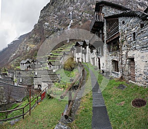 Traditional alpine village with many small wooden and stone houses and a mountain waterfall backdrop