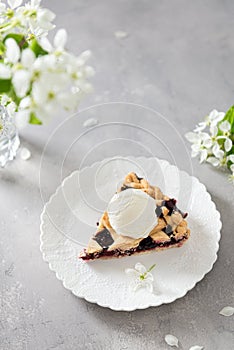 Traditional American cherry pie with an ice cream scoop on white plate on gray background with flowers. Side view, copy space.