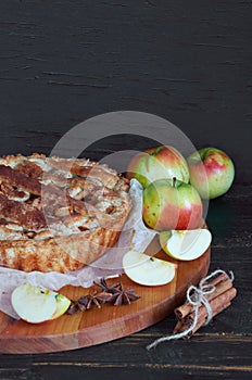 Traditional apple pie with spices on the brown wooden board. Apple pie decorated with sliced fresh apples and cinnamon sticks