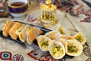 Traditional Arabic kataif crepes stuffed with cream and pistachios, prepared for iftar in Ramadan on paisley background