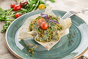 Traditional Arabic Salad Tabbouleh with couscous, tomato and greens in lavash bread bowl on wooden table