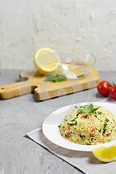 Traditional Arabic salad or Tabbouleh on white plate, healthy vegetarian dish with couscous on cement background