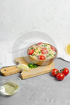 Traditional Arabic salad or Tabbouleh in wooden bowl, healthy vegetarian dish with couscous on cement background