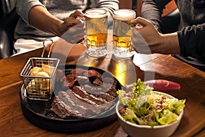 Traditional Argentinian barbecued meat and salad with people drinking beer in the background