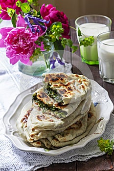 Traditional Armenian flatbread with greens zhengyalov hats, served with yogurt on the background of a bouquet.