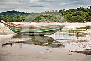 Traditional Asian boat on shoal during low tide on tropical beach in overcast day