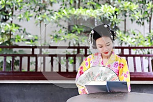 Traditional Asian Japanese beautiful Geisha woman bride wears kimono hold a fan reading book in a summer nature