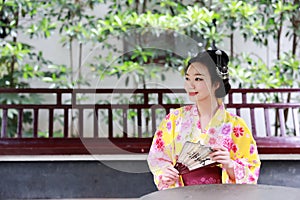 Traditional Asian Japanese beautiful Geisha woman bride wears kimono hold a fan reading book in a summer nature