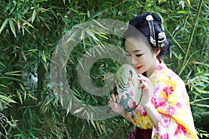 Traditional Asian Japanese beautiful Geisha woman bride wears kimono hold a fan in a summer nature