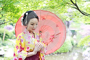 Traditional Asian Japanese beautiful Geisha woman bride wears kimono hold a red umbrella in a summer nature