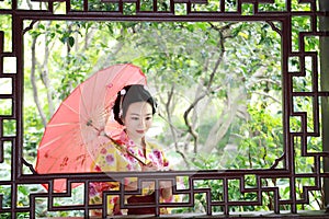 Traditional Asian Japanese beautiful Geisha woman bride wears kimono with red umbrella on hand in a summer nature