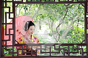 Traditional Asian Japanese beautiful Geisha woman bride wears kimono with red umbrella on hand in a summer nature