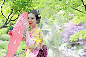 Traditional Asian Japanese beautiful Geisha woman wears kimono bride with a red umbrella in a graden