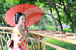 Traditional Asian Japanese beautiful Geisha woman wears kimono bride with a red umbrella in a graden