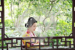 Traditional Asian Japanese beautiful Geisha woman wears kimono with a fan on hand in a summer nature