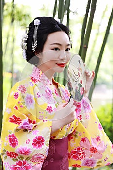 Traditional Asian Japanese beautiful Geisha woman wears kimono hold a fan on hand in a summer graden