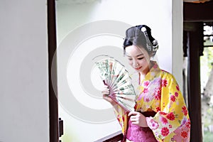 Traditional Asian Japanese beautiful Geisha woman wears kimono hold a fan sit in a summer nature garden