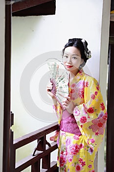 Traditional Asian Japanese beautiful Geisha woman wears kimono hold a fan sit in a summer nature garden