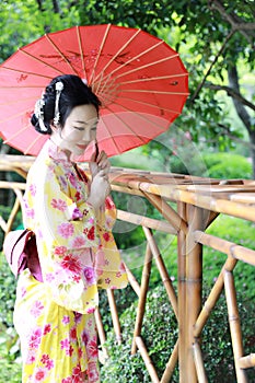 Traditional Asian Japanese beautiful Geisha woman wears kimono hold a umbrella on hand in a summer graden