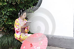 Traditional Asian Japanese beautiful Geisha woman wears kimono hold a umbrella reading book in a summer nature