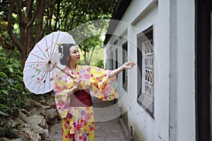 Traditional Asian Japanese beautiful Geisha woman wears kimono hold a white red umbrella in a summer nature garden