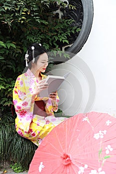 Traditional Asian Japanese beautiful Geisha woman wears kimono reading book in a summer nature