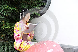 Traditional Asian Japanese beautiful Geisha woman wears kimono reading book in a summer nature