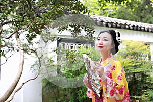 Traditional Asian Japanese beautiful Geisha woman wears kimono reading book in a summer nature