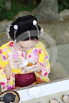 Traditional Asian Japanese beautiful Geisha woman wears kimono show tea art ceremony drink tea in a summer spring outdorr garden