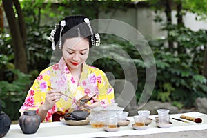 Traditional Asian Japanese beautiful Geisha woman wears kimono show tea art ceremony drink tea in a summer spring outdorr garden