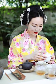 Traditional Asian Japanese beautiful Geisha woman wears kimono show tea art ceremony drink tea in a summer spring outdorr garden