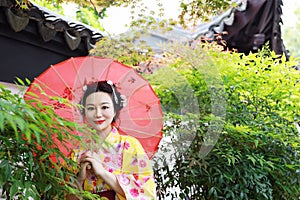 Traditional Asian Japanese beautiful woman bride wears kimono with red umbrella in front of a temple in outdoor spring garden