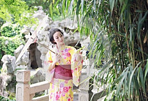 Traditional Asian Japanese beautiful woman bride wears kimono with white umbrella stand by bamboo in outdoor spring garden