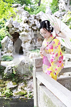 Traditional Asian Japanese beautiful woman bride wears kimono with white umbrella stand by bamboo in outdoor spring garden