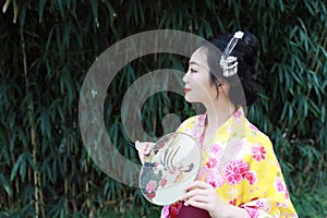 Traditional Asian Japanese beautiful woman with a fan on hand stand by bamboo in a garden